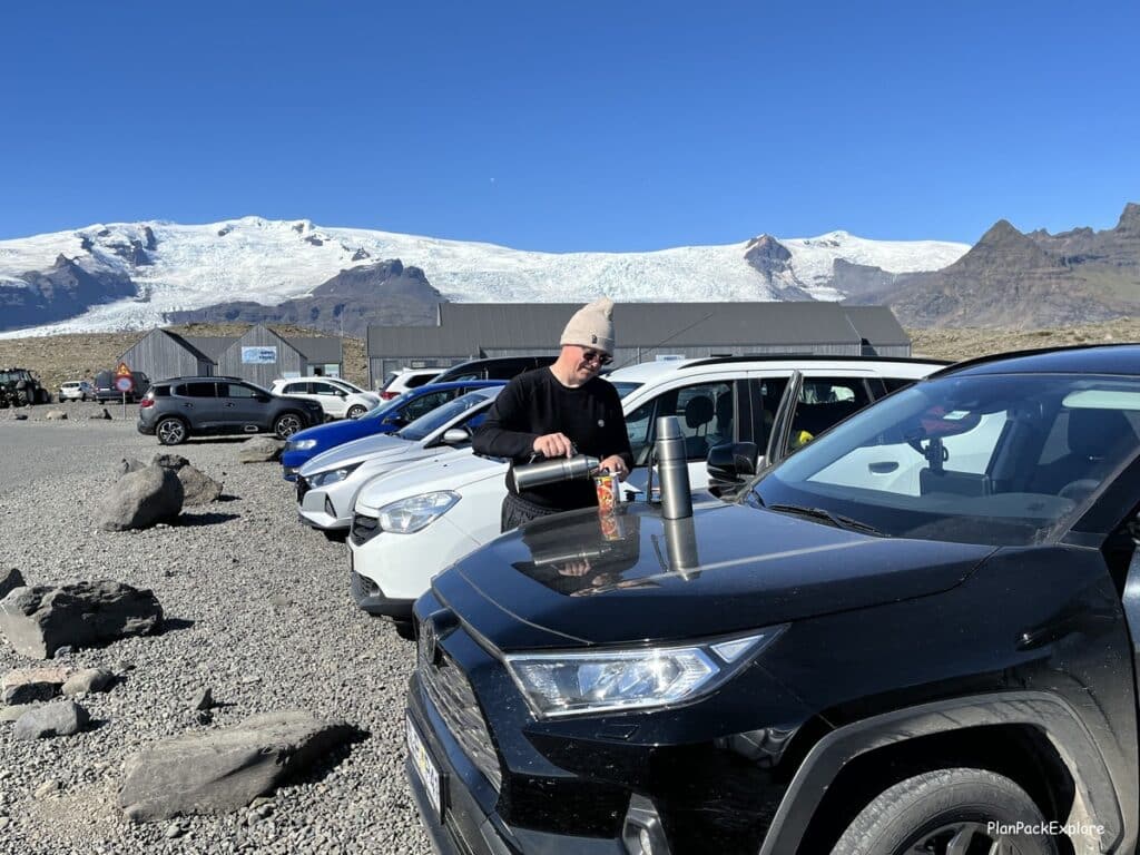 A man pouring water out of a thermos into a cup on the hood of the car at Fjallsárlón Lagoon parking lot in Iceland.