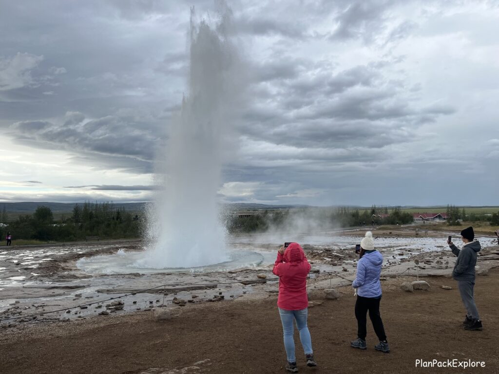 Family watching Strokkur geyser erupting at Geysir Hot Springs in Iceland.