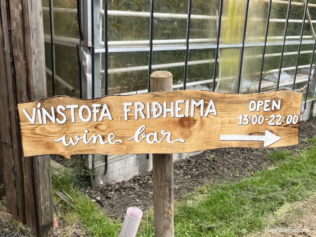 A wooden sign for the Wine Bar with directions and opening hours at Fridheimar Tomato Farm in Iceland.