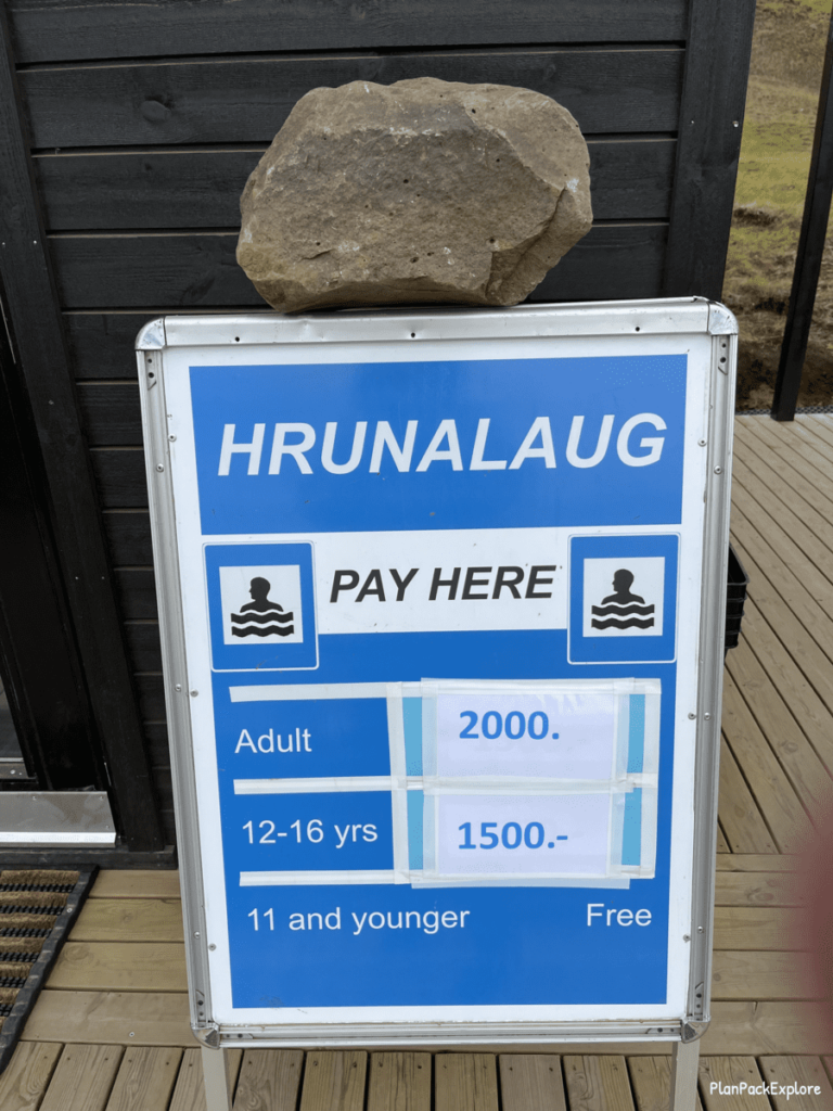 A blue sign with white letters stating the entry fees to Hrunalaug Hot Spring in Iceland.