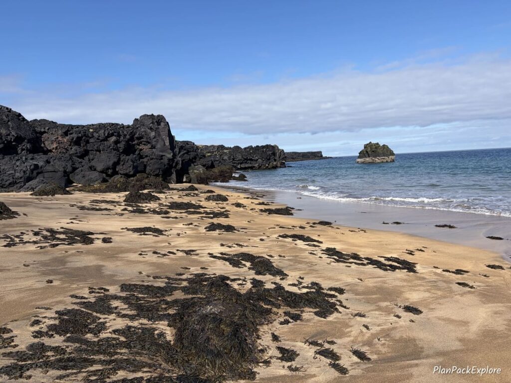 A golden sand beach and dark volcanic rocks on Snaefellsnes Peninsula in Iceland.