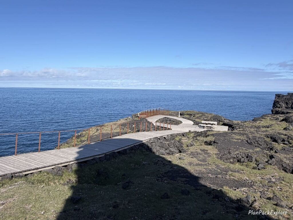 Wooden boardwalk near the ocean and Svortuloft lighthouse in Iceland.