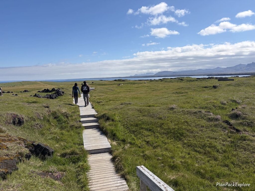 A vas grassy area and a wooden boardwalk near the Ondvendarnes lighthouse on Snaefellsnes Peninsula in Iceland.