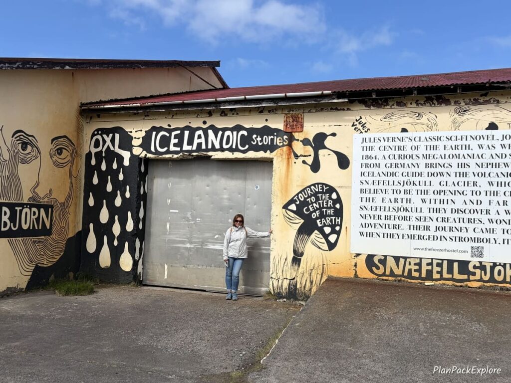 A person standing in front of a building covered in graffiti text on Snaefellsnes Peninsula in Iceland.