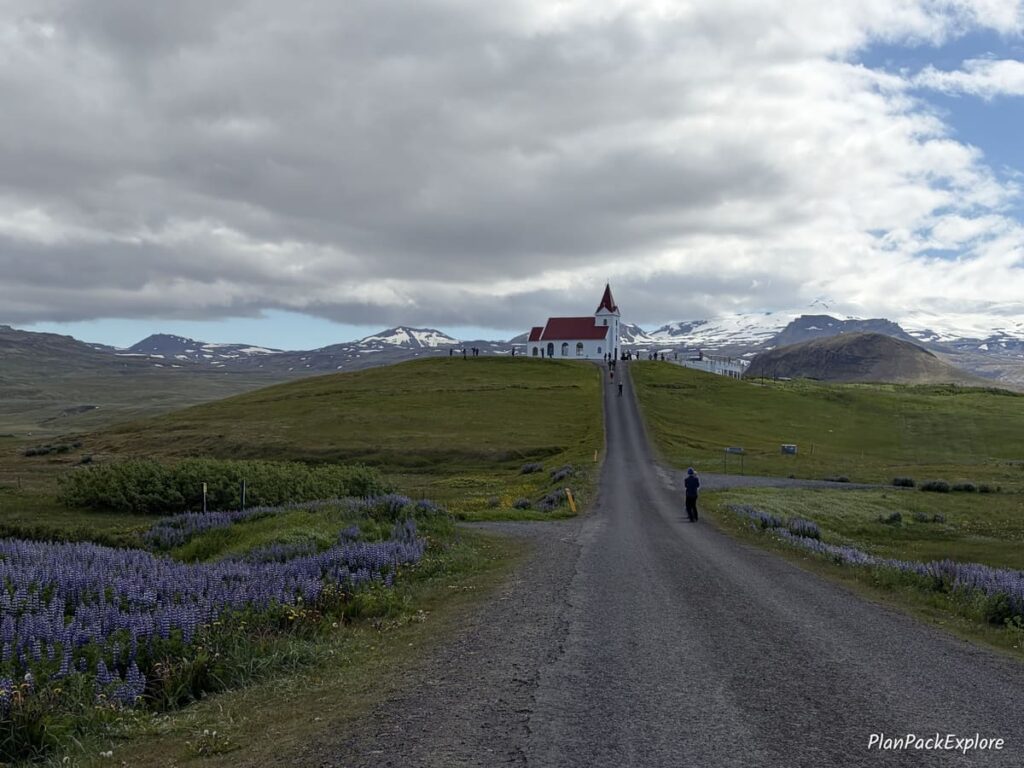 A white church with a red roof on a hill at the end of a paved roan on Snaefellsnes Peninsula in Iceland.
