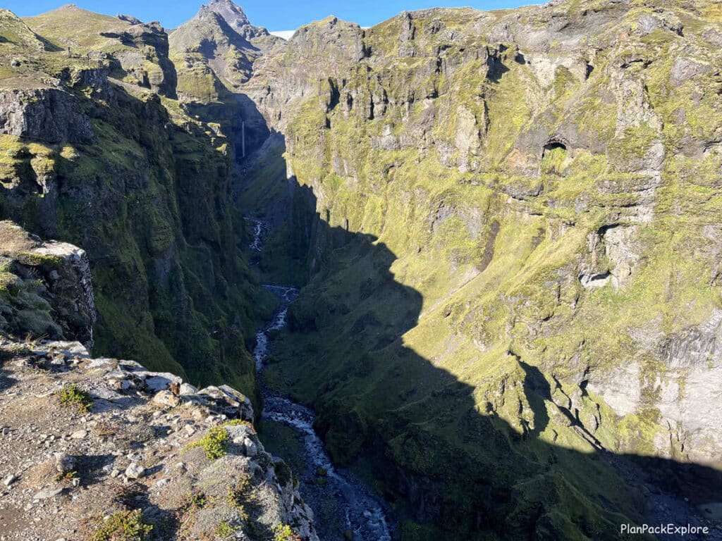 A deep moss-covered canyon with a river and a narrow waterfall in Iceland.
