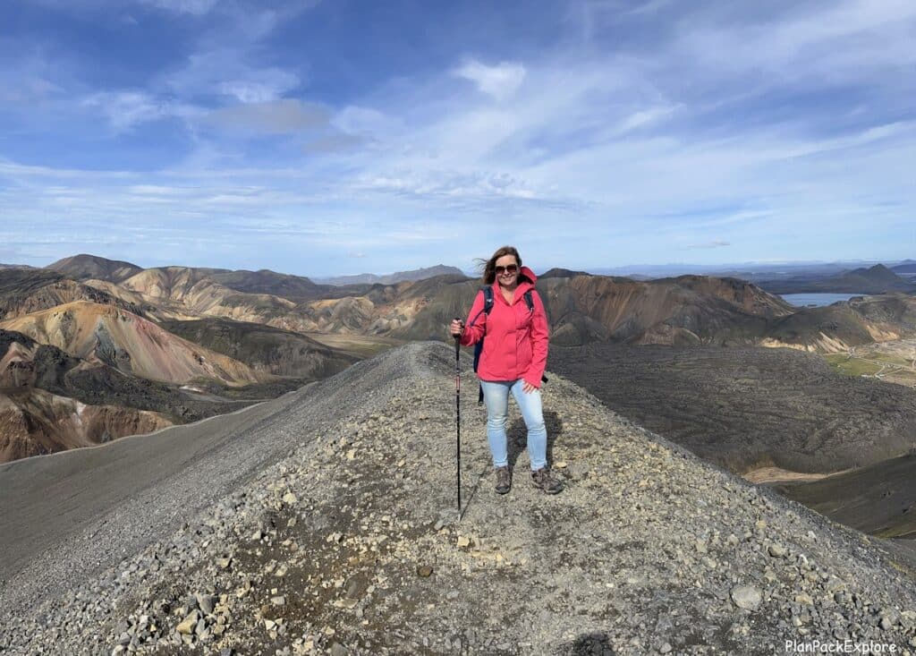 A person in a bright pink jacket standing on a rocky mountain ridge in Iceland.
