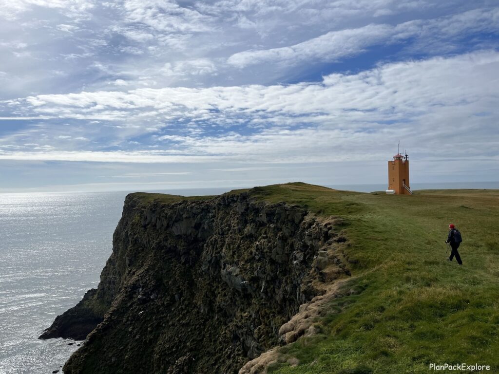 Ingolfshofdi promontory in Iceland. A green cliff and an orange lighthouse by the ocean.