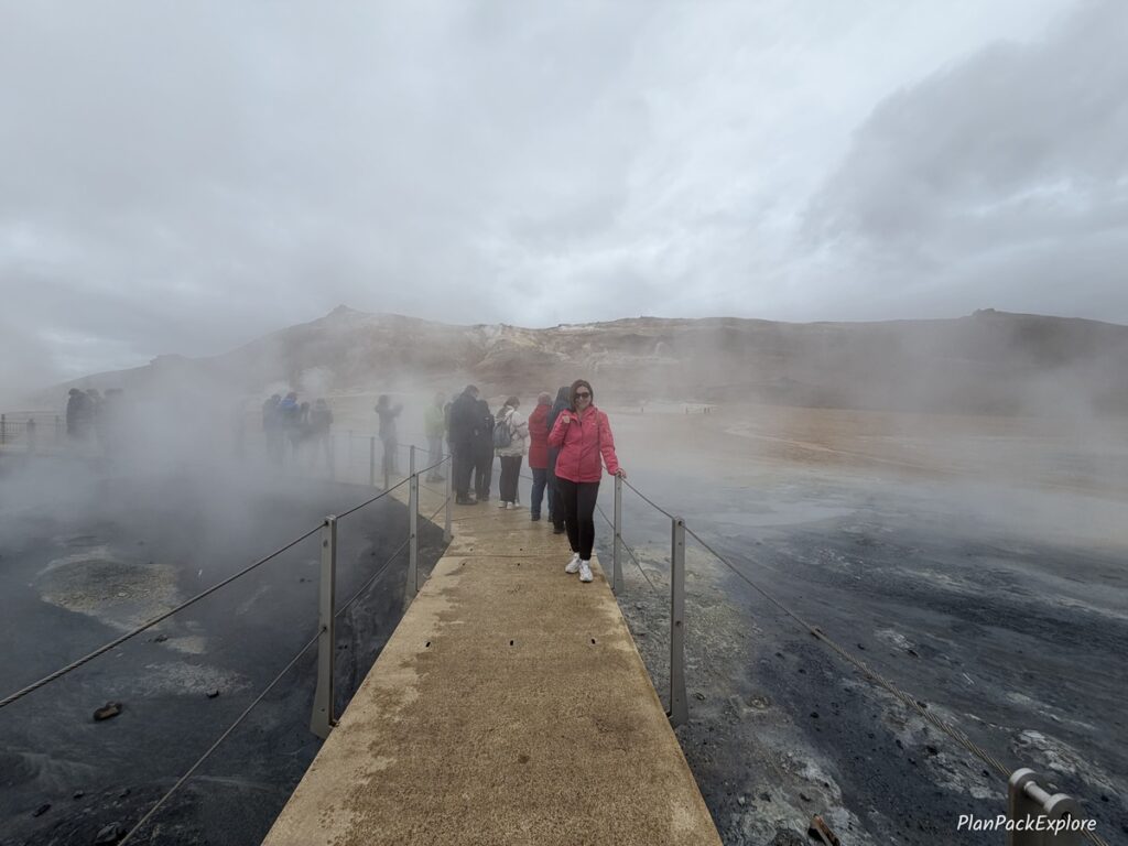 A person standing on a wooden boardwalk along Hverir Geothermal Area in Iceland.