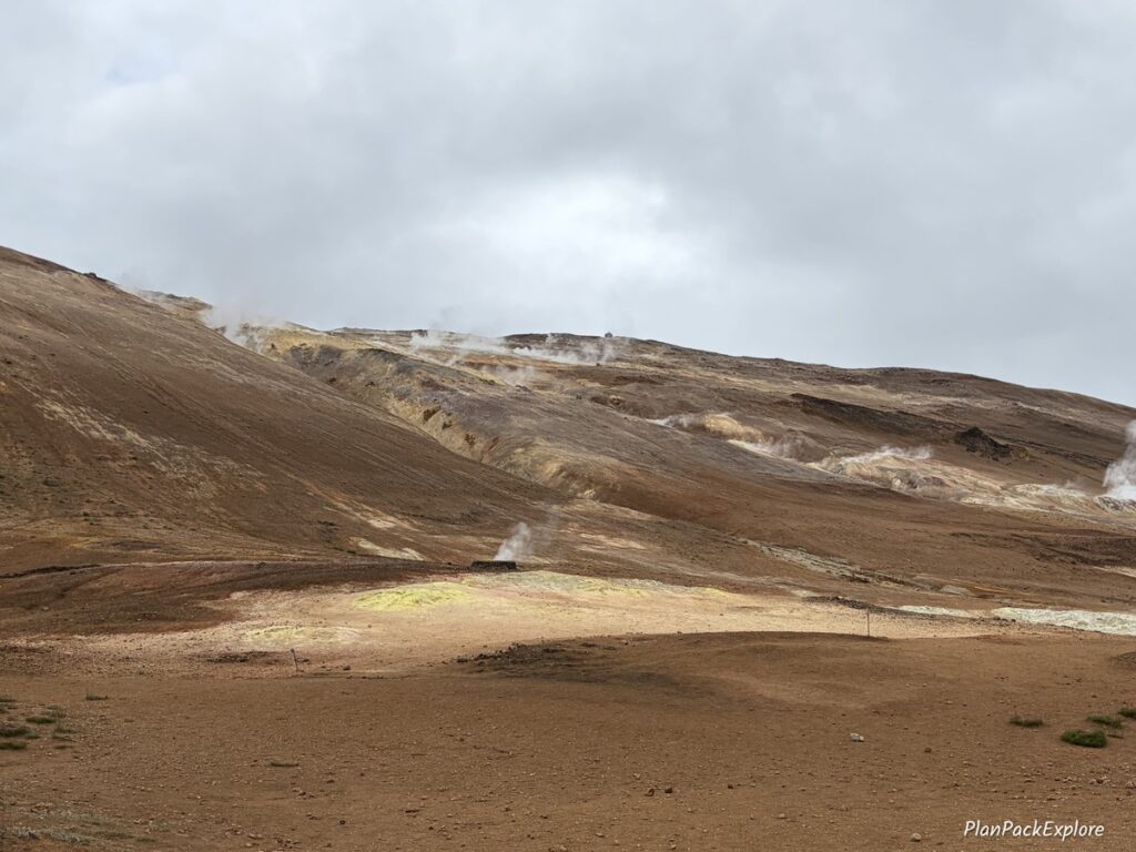 A rust-colored mountain with steam coming out of the cracks in the ground at Hverir Namafjall Geothermal Area in Iceland.