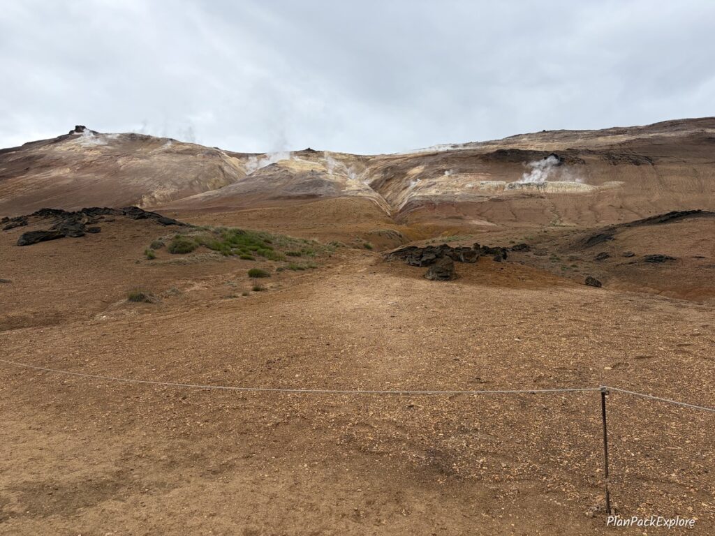 A rust-colored mountain with steam coming out of the cracks in the ground at Hverir Namafjall Geothermal Area in Iceland.