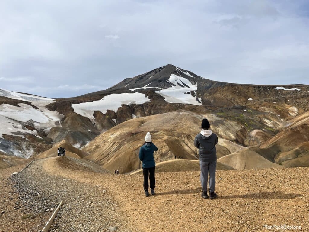 Two people standing at the edge of Hvaradalir valley in Kerlingarfjoll, Iceland, with the colorful mountains in the background.