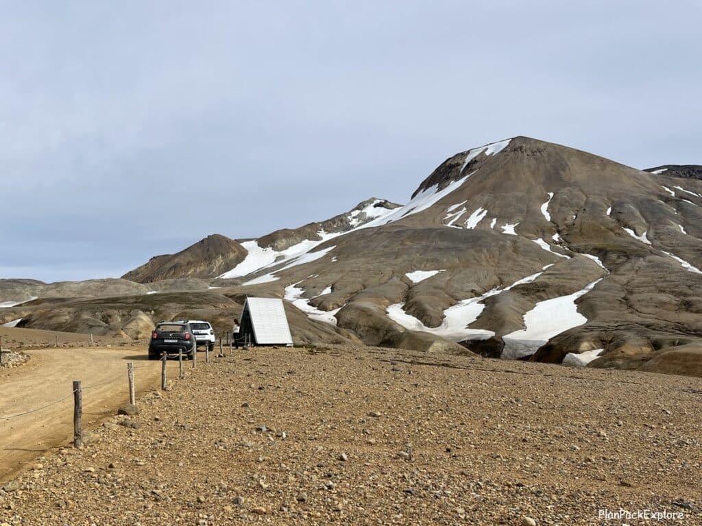 A view of a A-frame small building in Hveradalir Geothermal area in Iceland, with mountains in the background.