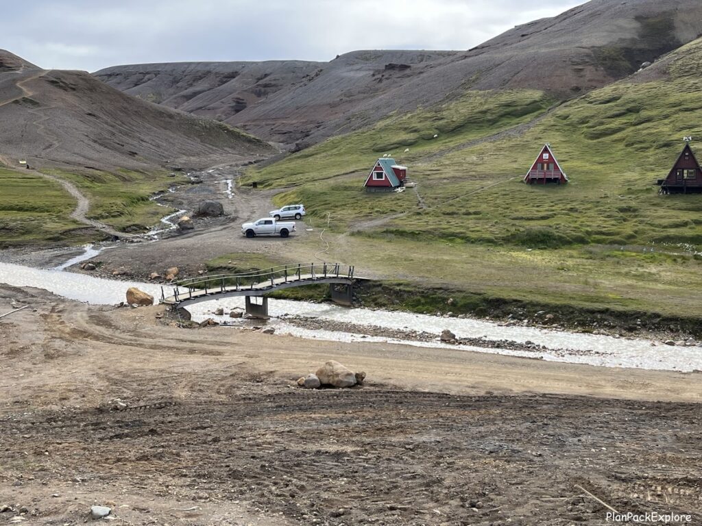 A bridge over a small river with A-frame huts in the background in Kerlingarfjoll, Iceland.