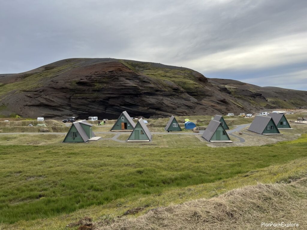 A grouping of A-frame small green huts in a field by Kerlingarfjoll mountains, Iceland.