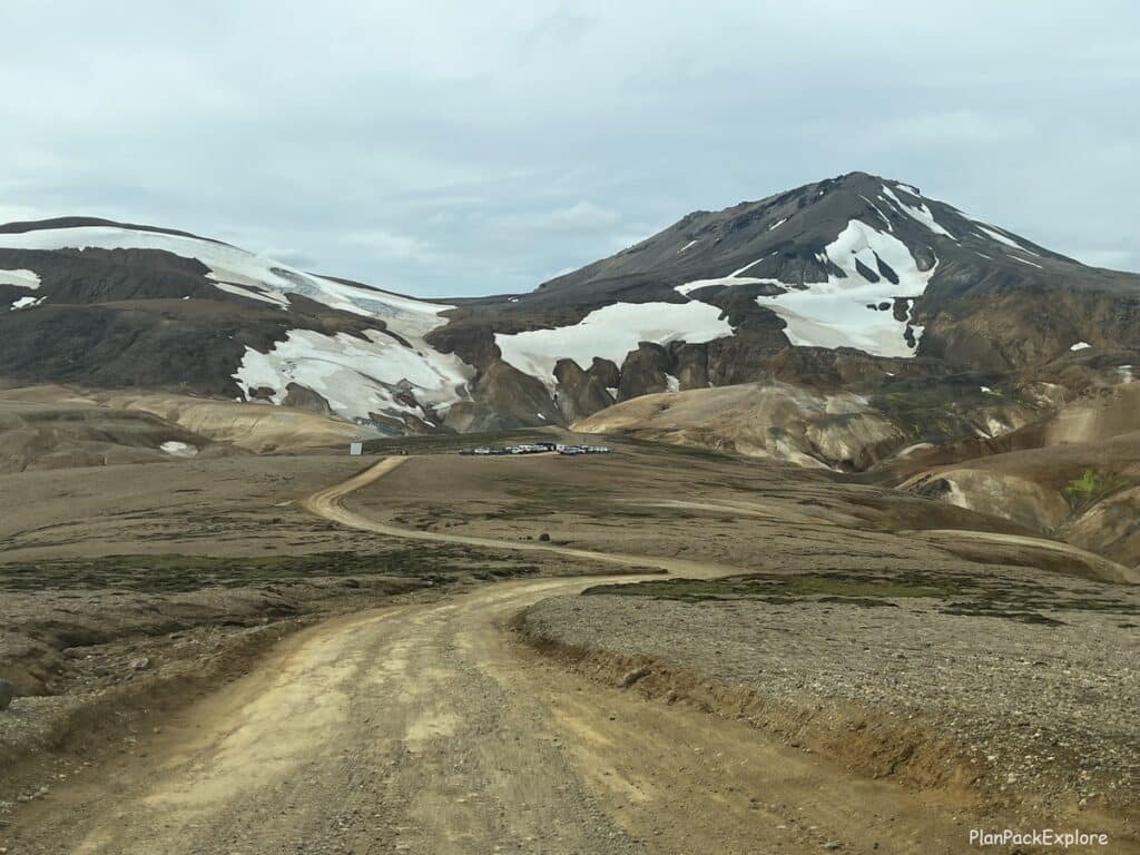 Drive to the Hveradalir parking lot in Kerlingaffjoll, Iceland - a dirt road, going downhill, with colorful, partially snow-covered mountains in the view.