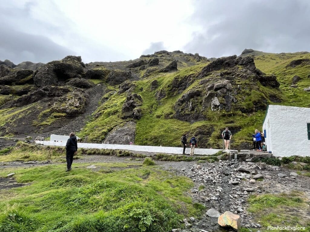 A side view of a geothermal pool and changing room building with a mountain in the background in Iceland.
