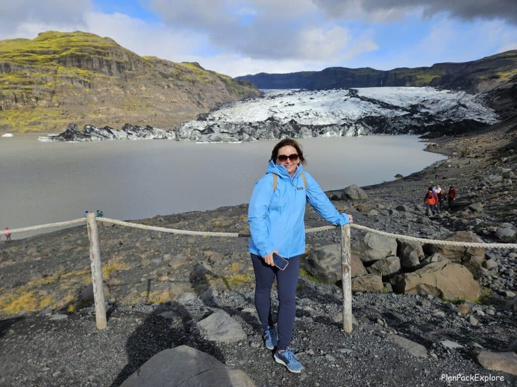 The bog author wearing a blue jacket standing on the viewing platform, with Solheimajokull glacier behind her (Iceland)