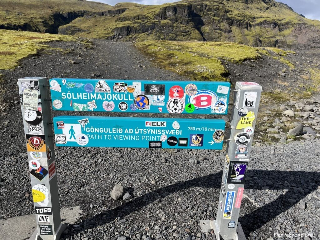 A light blue sign with white letters for a trail to the Solheimajokull glacier viewpoint in Iceland.