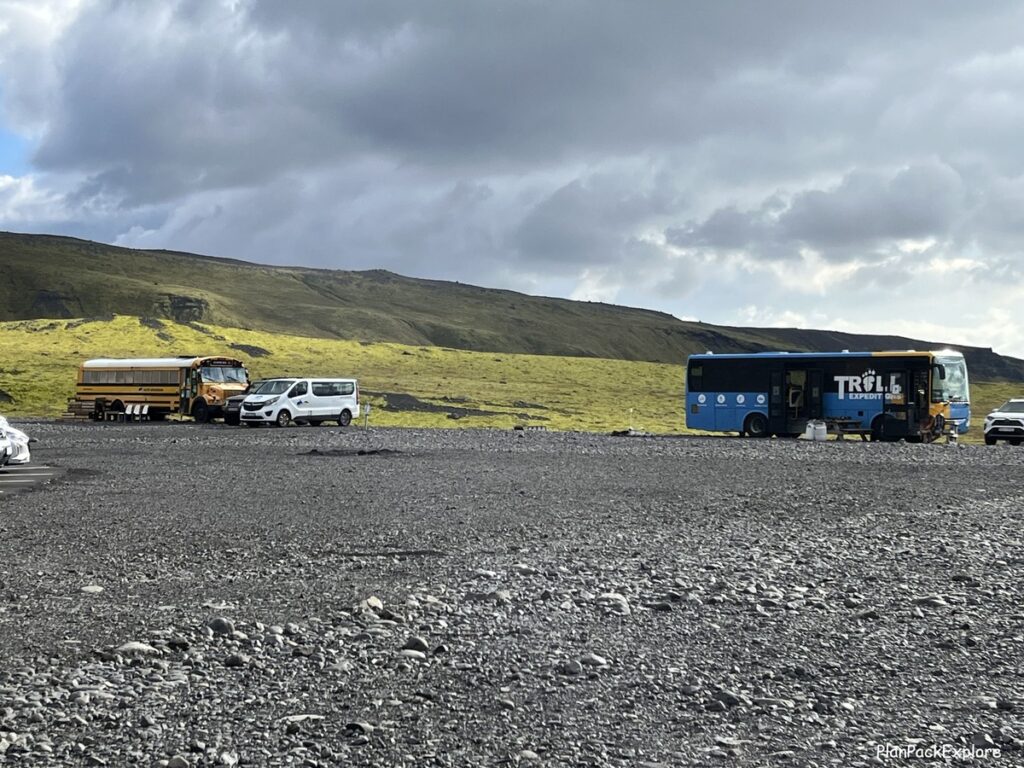 Two school buses (one yellow and one green) parked on a gravel lot of a parking area for Solheimajokull glacier in Iceland.