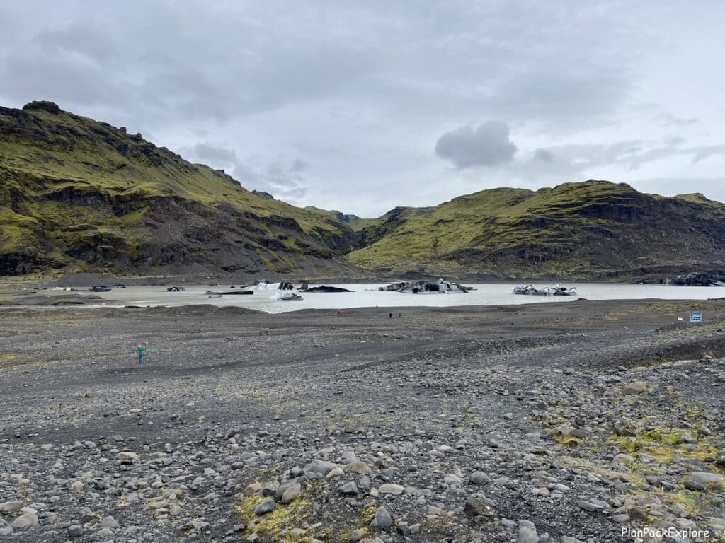 A view of the Solhheimajokull glacier lagoon in Iceland- a brown water lake with icebergs floating on top.