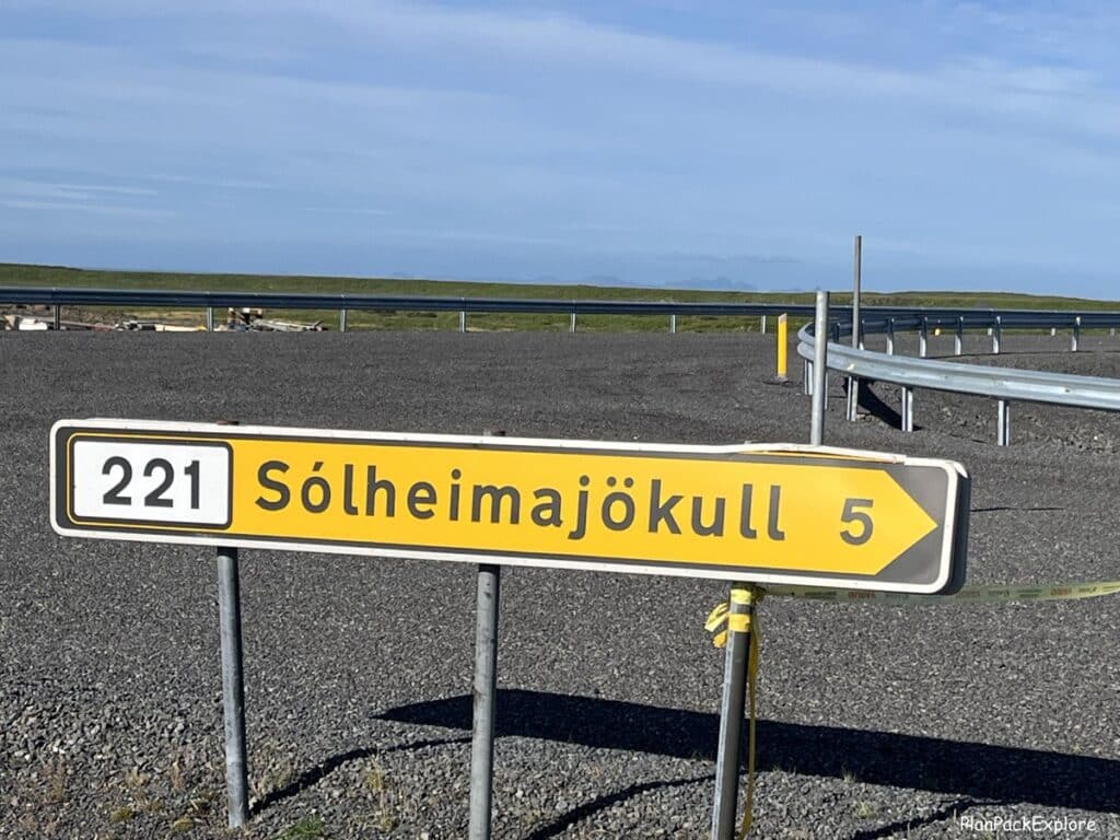 A road sign for the Solheimajokull glacier parking lot in Iceland. A long yellow sign with black letters.