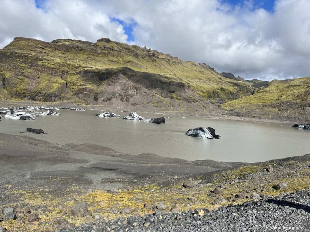 A view of the Solhheimajokull glacier lagoon in Iceland- a brown water lake with icebergs floating on top.