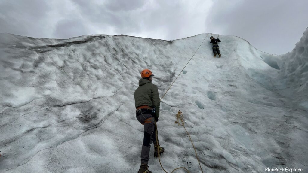 A person ice climbing on the Skaftafel glacier in Iceland. A guide is at the bottom of the climbing wall.