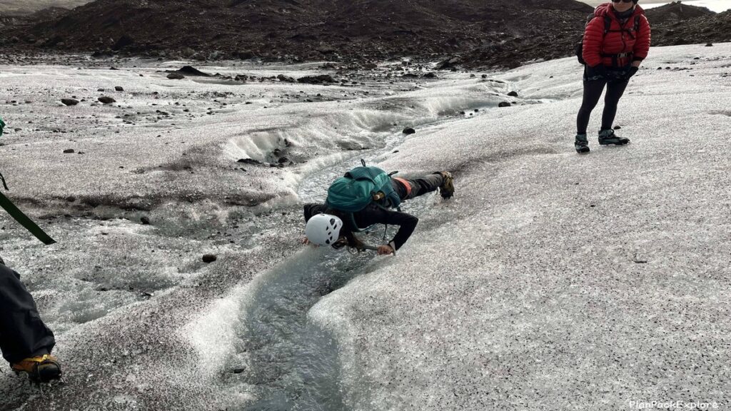A person doing a glacier push-up over a small glacial stream during a Vatnajokull ice climbing tour in Iceland.
