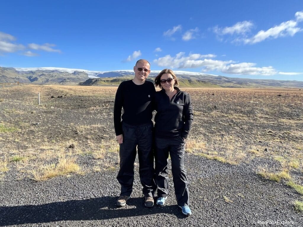 A couple standing on the gravel road with Solheimajokull glacier behind them.