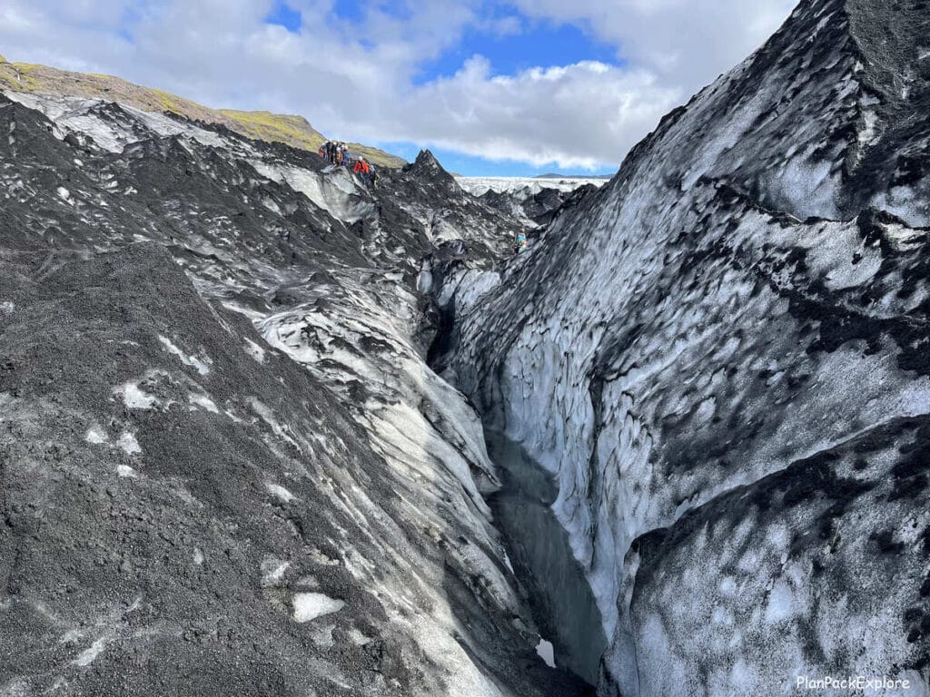 People hiking on Solheimajokull glacier in Iceland in the far distance. A large crevasse in the glacier visible in the front.