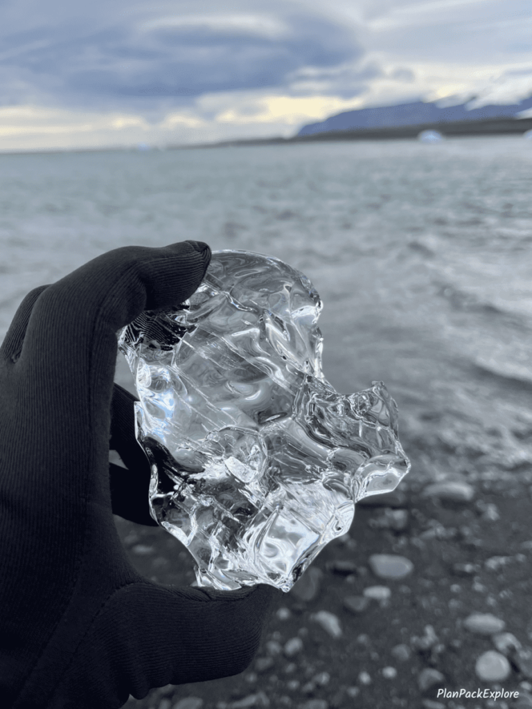 Clear iceberg held in a gloved hand at Diamond Beach in Iceland.
