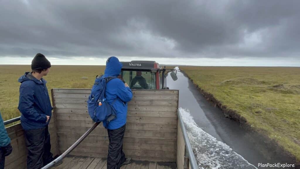 Two men in raincoats in a wagon during a tractor ride through a marsh in Iceland.
