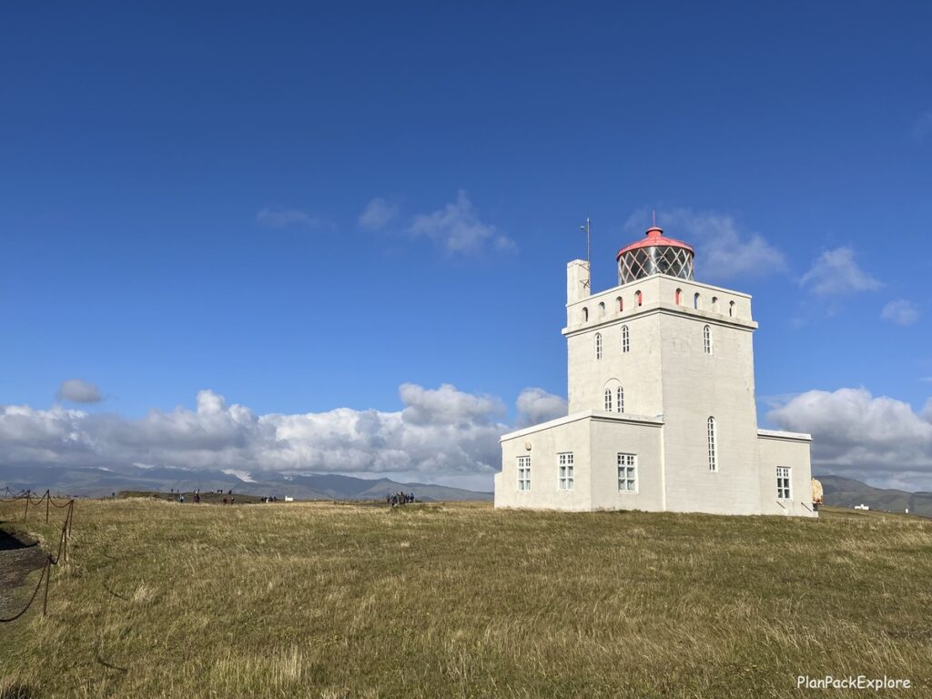 A white lighthouse with an orange beacon at dyrholaey cliffs in Iceland.