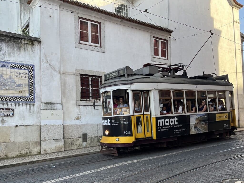A yellow tram next to a white building on a street in Lisbon, Portugal.