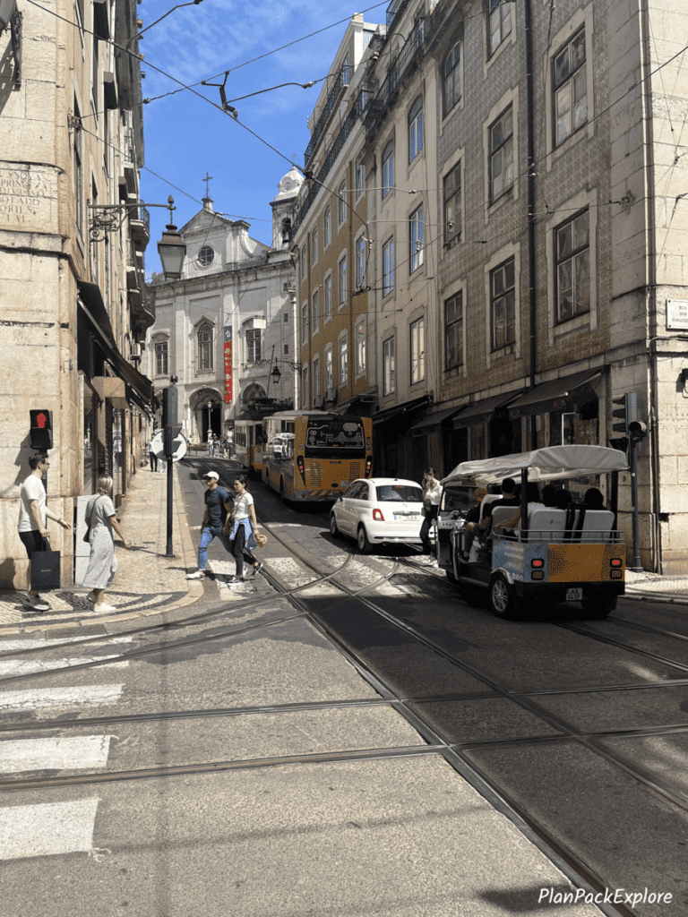 A narrow street with a bus, a car and a tuk tuk on the right side in Lisbon, Portugal.