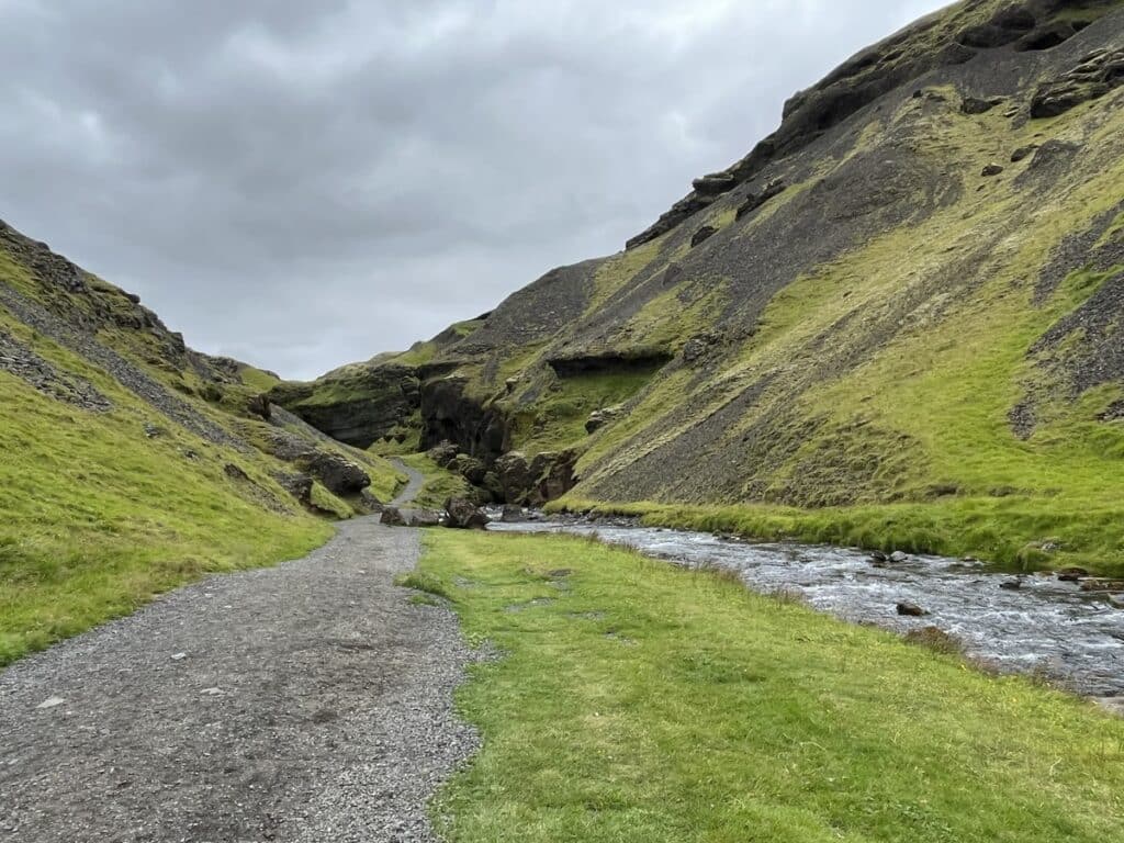 a wide gravel path in a lush green valley in Iceland.