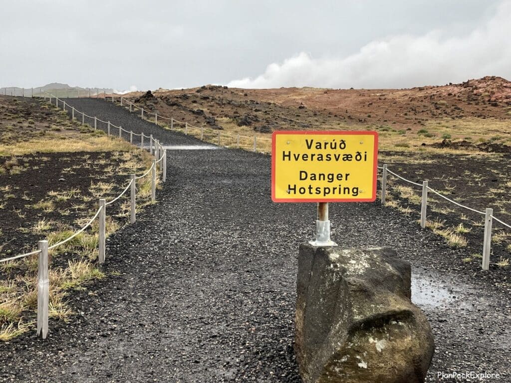 A yellow warning sign on a gravel path at gunnuhver hot spring at Gunnuhver geothermal area on reykjanes peninsula in Iceland.