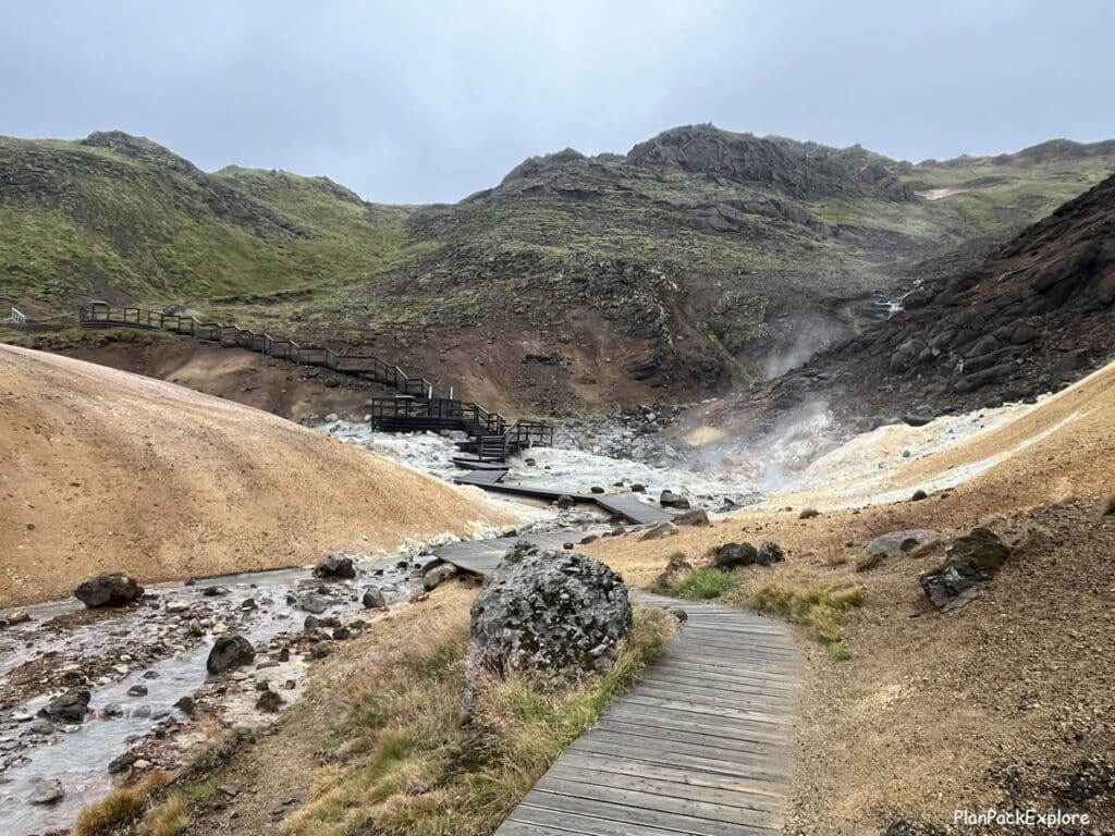 A steaming hot spring and a wooden boardwalk and stairs in Seltun geothermal area on reykjanes peninsula in Iceland.