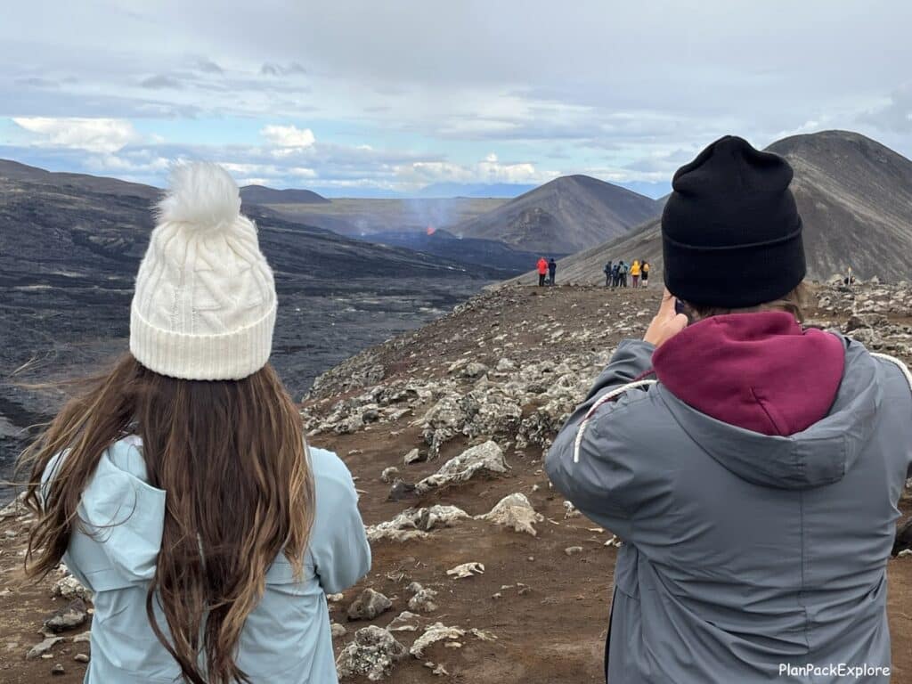 Two people in hats watching lava erupting from a volcanic crater on reykjanes peninsula in Iceland.