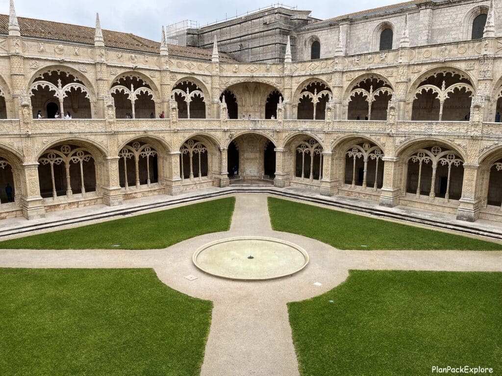 Stone convent cloister next to a grass courtyard at Jeronimos Monastery in Lisbon, Portugal.