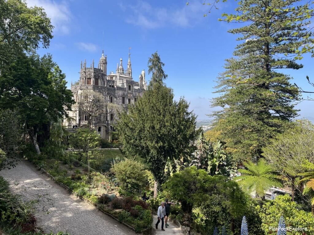 A stone palace with spiked towers visible through the trees at Quinta da Regaleira in Sintra, Portugal.