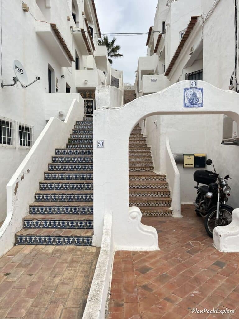 A staircase decorated with colorful tiles next to an arch on a street in Carvoeiro, Portugal.