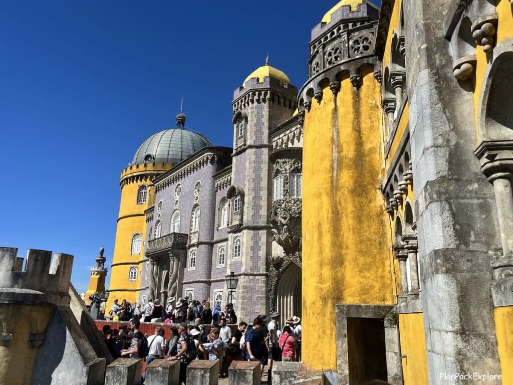 Yellow and tiled walls of Pena Palace in Sintra, Portugal, with a crowd of people in front of it.