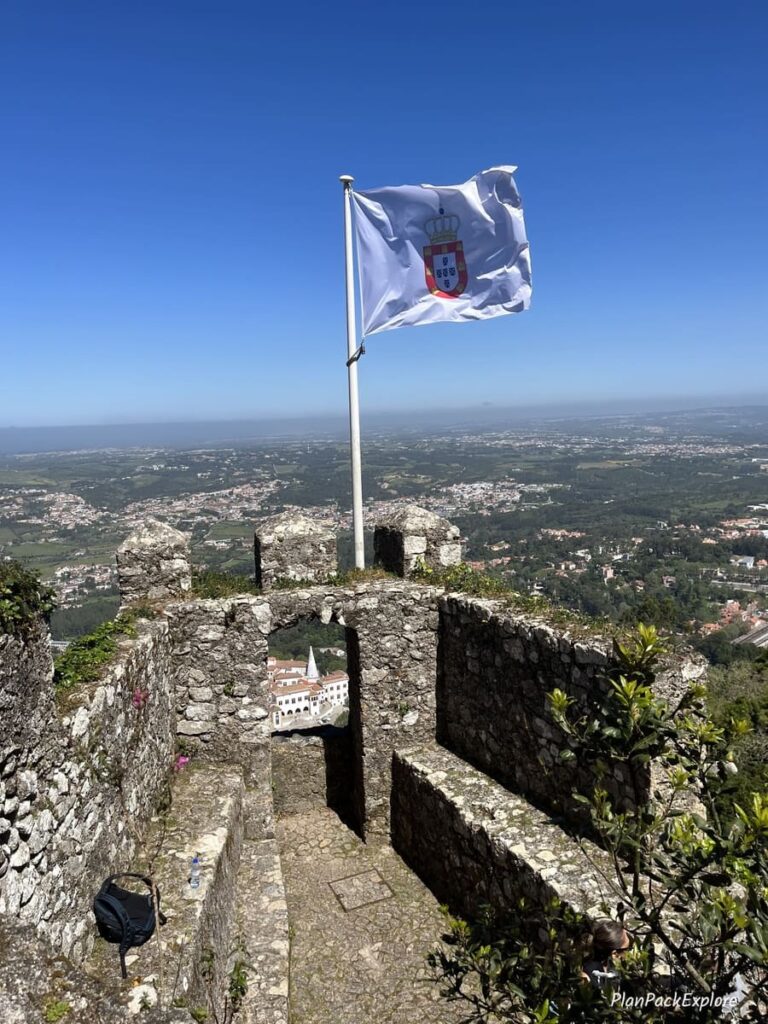 Stone viewpoints with a white flag at the Moorish Castle in Sintra Portugal, also showing views of the surrounding area.
