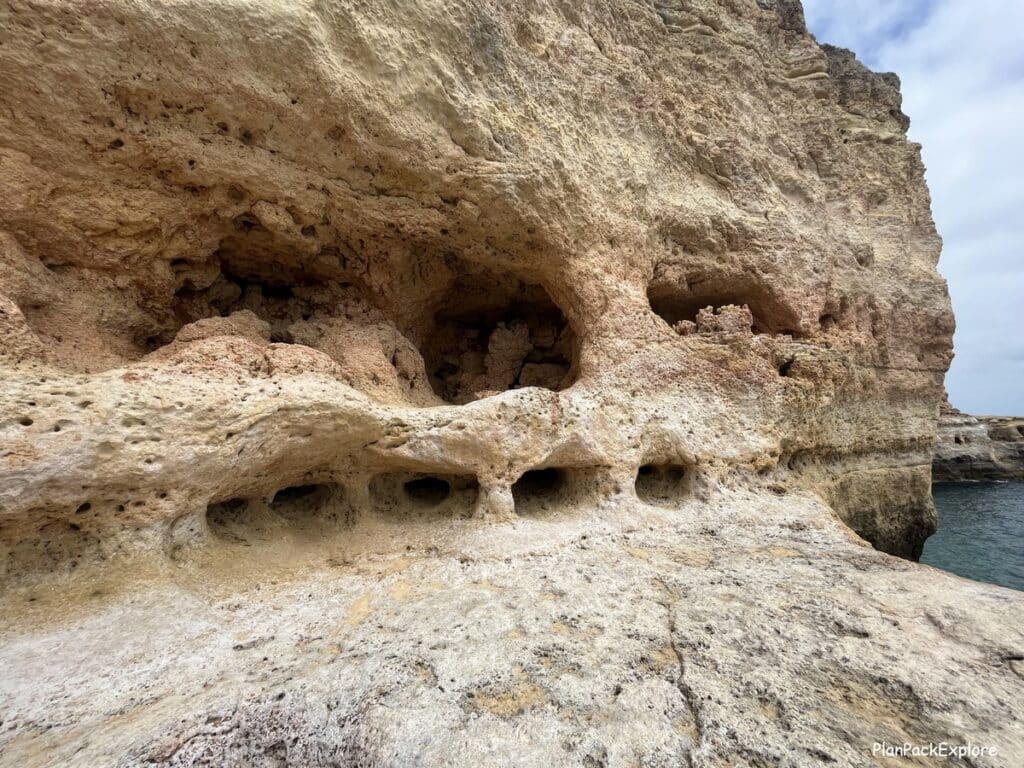 A natural cave with a row of smaller caves below carved in a cliff near the Carvoeiro boardwalk in Portugal.