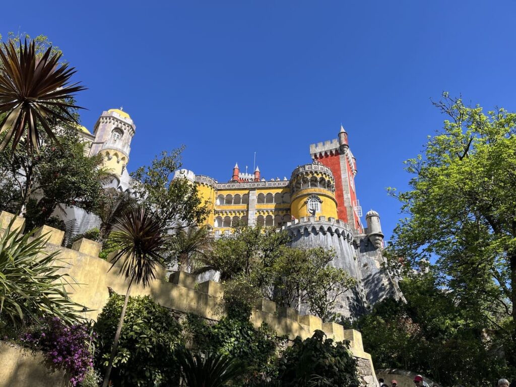 A view of yellow and cream Pena palace towers through the tree branches in Sintra, Portugal.