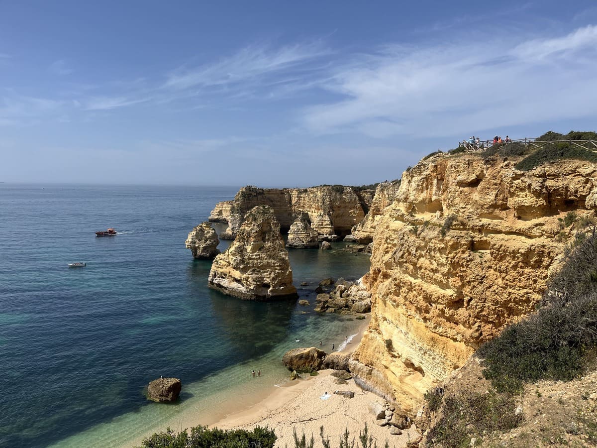 Golden colored limestone cliffs over blue ocean water and a beach at the Seven hanging Valleys trail in the Algarve, Portugal.