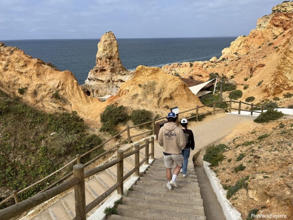 Two people walking down the stairs toward limestone rock formations at algar seco in the algarve, portugal.