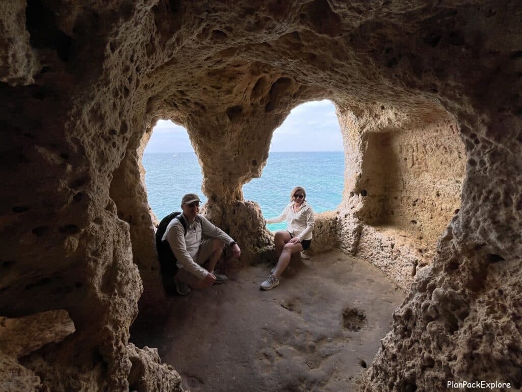 two people sitting inside a cave with two rocky hollowed out windows shaped like the eyes of a doll at Algar Seco in the Algarve, Portugal.